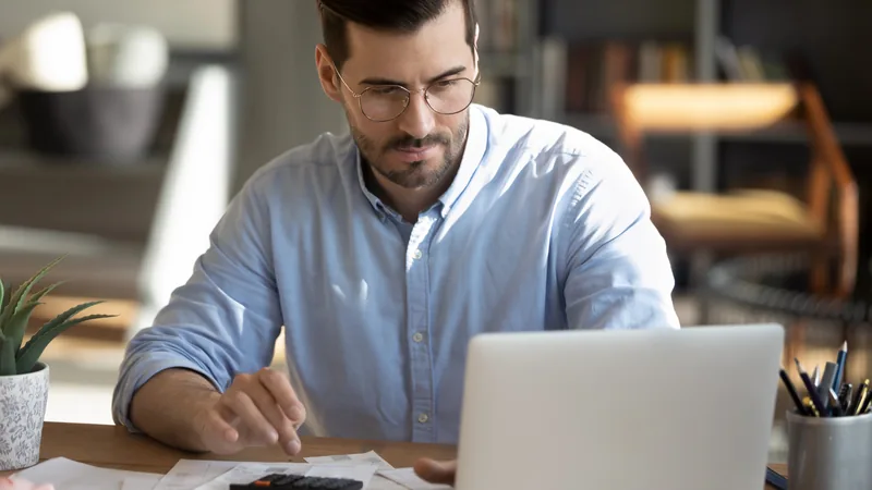 A man in glasses working through paperwork at a laptop