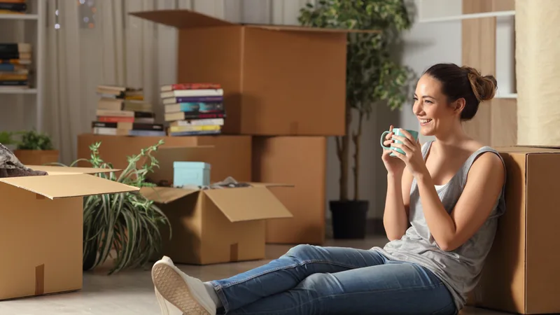 A woman sitting among moving boxes with a cup of coffee in her new home