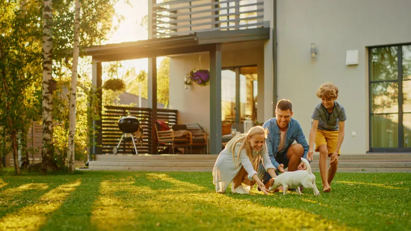 A family playing with their dog on the lawn in front of a modern home at sunset